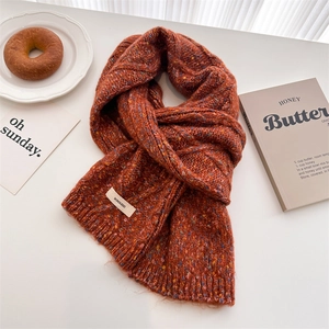 Orange chunky knit wool scarf with colorful flecks and brand label on white background