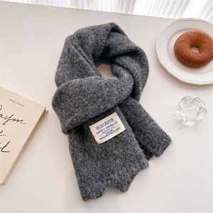 Detail showing thick chunky knit texture of a gray wool scarf with a woven label
