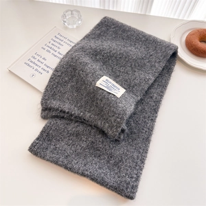 Detailed view of gray knit wool scarf with a brand label on a cozy decorative setup