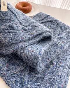 Detailed close-up of blue confetti wool knit scarf with cable pattern and brand label