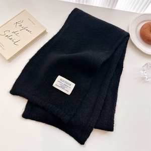 Close-up of black knitted scarf with brand label on minimalist winter lifestyle setting