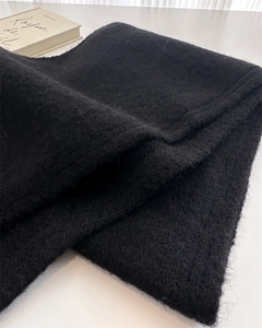 Close-up of black wool knit scarf texture showing soft plush fibers on white desk