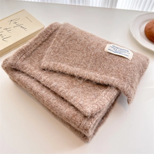 Detail of taupe wool knit scarf with brand label on a cozy white aesthetic background