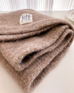 Close-up of beige knit scarf texture with a white woven label and soft fabric detail