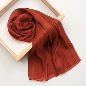 Detailed view of rust red silk scarf with satin luster draped over a wooden frame