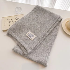 Detail of grey wool knit scarf with premium fabric label on elegant white tabletop
