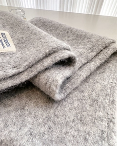 Close-up of thick light gray wool knit scarf showing soft brushed texture and brand tag