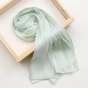 Close-up of light green silk scarf with pearl luster texture on wooden frame background
