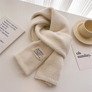 Detail view of cream knit scarf texture with brand label on a cozy white desk setup
