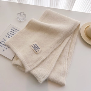 Close-up of cream knit scarf texture with vintage woven label on white background