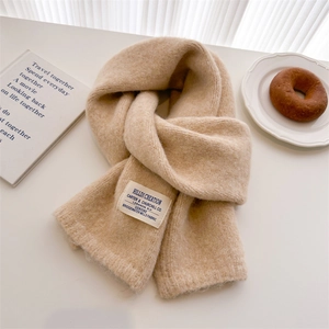 Detail shot of beige wool knitted scarf with a textile label on a clean aesthetic background