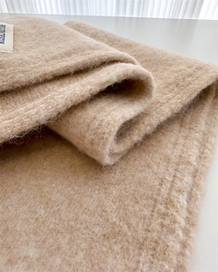 Close-up of oatmeal wool scarf fabric showing soft texture and premium brand label