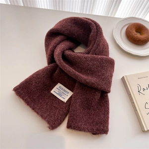Detailed close-up of thick wine red wool knit scarf with a white rectangular vintage label