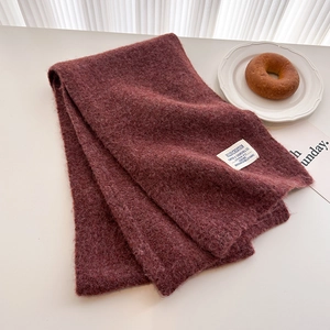 Detailed texture of burgundy thick knit scarf with vintage white fabric label on table