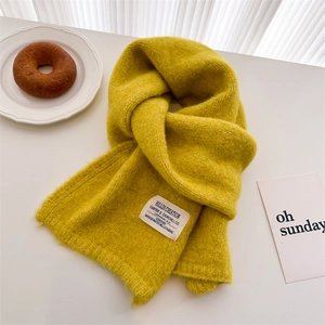 Detail of ginger yellow knitted mohair scarf with fabric tag on a cozy table setting
