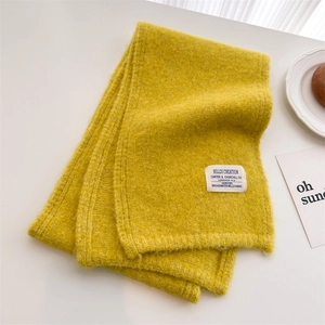 Close-up of mustard yellow knitted wool scarf with a woven textile brand label detail