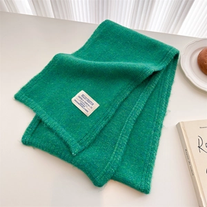 Close-up of emerald green knit scarf texture with a white square brand tag detail