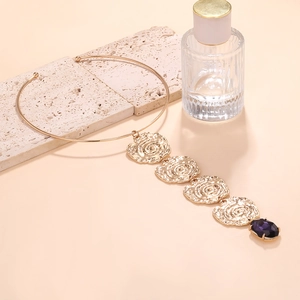 Detailed shot of golden coin pendant necklace with purple gemstone on stone