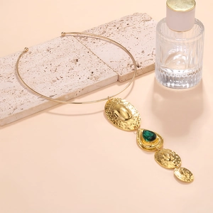Detail of golden geometric necklace with hammered texture and green teardrop pendant