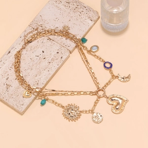 Layered gold necklace with sun, moon, and heart charms on a beige travertine stone