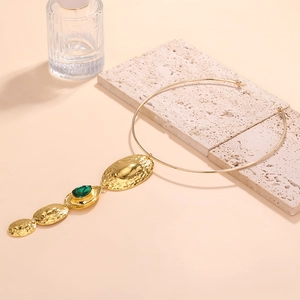 Detail of hammered gold pendants with a vibrant green teardrop gemstone on collar necklace