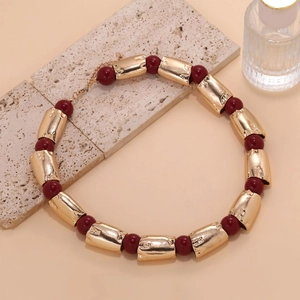 Exaggerated geometric necklace with gold cylinders and red beads on a neutral base