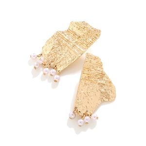 Close-up of golden geometric earrings with hammered texture and small white pearls