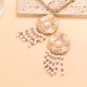 Golden flower drop earrings with faux pearl tassels on a minimalist stone background