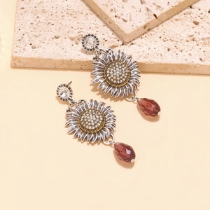 Macro detail of silver sunflower earrings featuring inlaid rhinestones and red teardrop charms