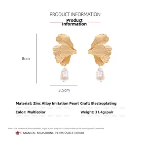 Detailed close-up of golden ginkgo leaf earrings with irregular imitation pearl drop