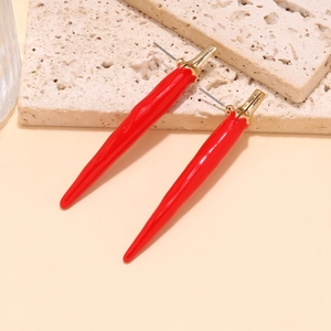 Détail macro de boucles d'oreilles piment en émail rouge sur pierre beige texturée