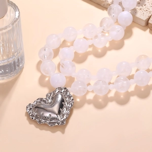 Gros plan du pendentif cœur argenté avec texture et perles blanches laiteuses