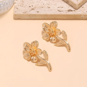 Elegant gold flower earrings with brushed texture and petal detail on stone background