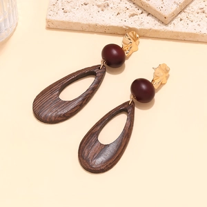 Close-up of geometric hollow wooden teardrop earrings with gold hammer-textured studs