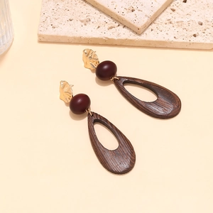Macro view of teardrop wood pendant earring with gold metal and deep red resin bead