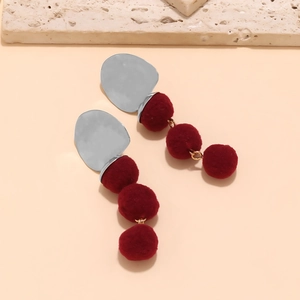 Close-up of geometric earrings with silver metal plates and three deep red pompoms