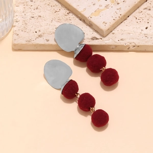 Detail of fashion drop earrings with silver metal and three deep red plush pom-poms