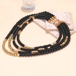 Multilayer beaded waterfall necklace with black and gold beads on a minimalist display