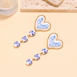 Detailed view of long heart earrings with blue floral ceramic beads and gold chain tassels