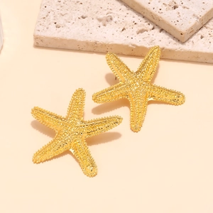 Détail de boucles d'oreilles étoile de mer dorées avec texture grainée sur pierre beige