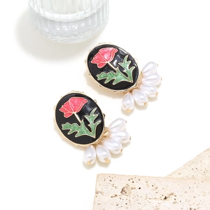Close-up of enamel rose earrings with dangling pearls on a textured stone surface