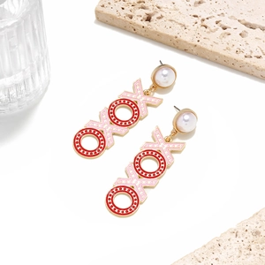 Detail of gold XOXO earrings with pink enamel, pearl studs, and textured stone background