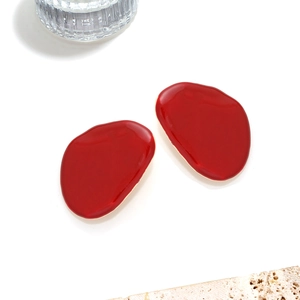 Detailed macro view of red enamel pebble earrings with polished gold metallic edges