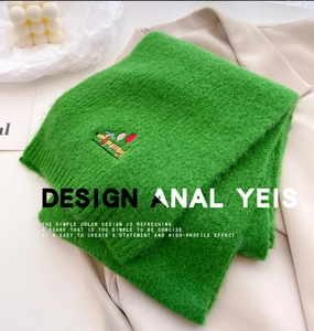 Detailed view of green knit scarf with embroidered dachshund puppy pattern and soft texture
