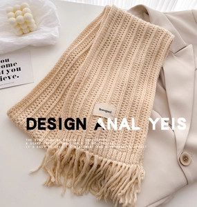 Detail of beige knit wool scarf with tassel fringe and brand label on cream blazer