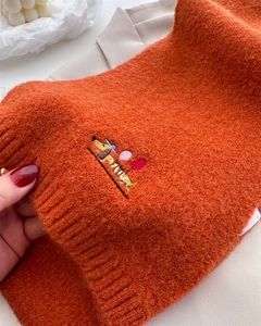 Detail of dachshund embroidery on chunky orange knit scarf with thick wool texture