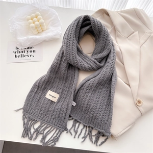 Detail of gray chunky knit wool scarf with tassel fringe and minimalist brand label