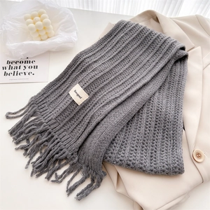 Detail of grey cable knit wool scarf with tassels and brand label on a suit