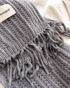 Detail of grey cable knit wool scarf with long fringe tassels and brand logo label