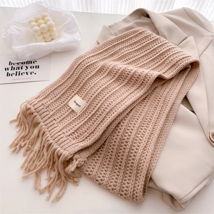 Detailed view of beige knit scarf with soft tassels and minimalist square brand label